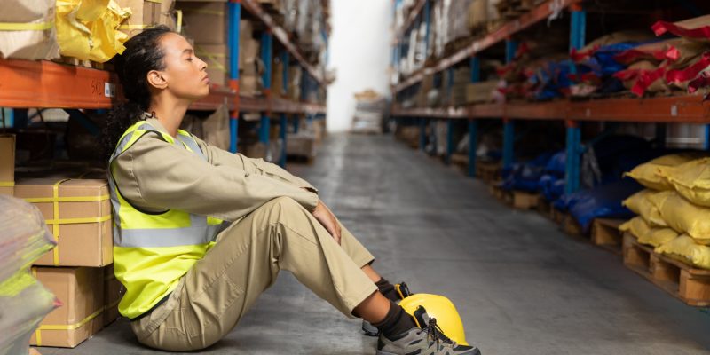 Tired female staff sitting with eyes closed in warehouse.